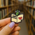 przypinka mól książkowy w dłoni na tle biblioteki